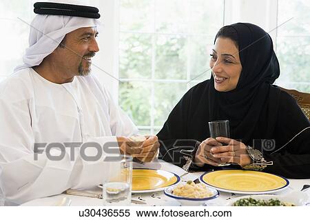 Stock Photography - Couple sitting at dinner table smiling (high key). Fotosearch