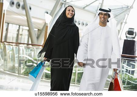 Couple walking in mall holding hands and smiling (selective focus) View Large Photo Image Stock Photograph - Couple walking in mall holding hands and smiling (selective focus). Fotosearch