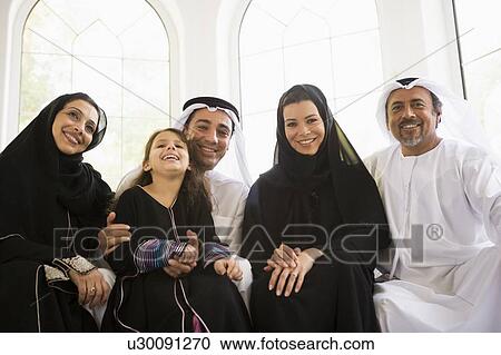 Stock Image - Family sitting in living room smiling (high key/selective focus). Fotosearch