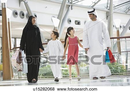 Stock Photo - Family walking in mall holding hands and smiling (selective focus). Fotosearch
