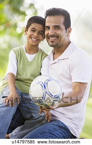 Stock Photography - Father and son outdoors in park with ball smiling (selective focus). Fotosearch