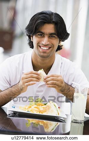 Man at restaurant eating sandwich and smiling (selective focus) View Large Photo Image Picture - Man at restaurant eating sandwich and smiling (selective focus). Fotosearch