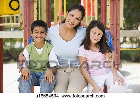 Mother and two young children sitting on playground structure smiling (selective focus) View Large Photo Image Picture - Mother and two young children sitting on playground structure smiling (selective focus). Fotosearch