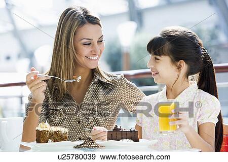 Stock Photo - Mother at restaurant with daughter eating dessert and smiling (selective focus). Fotosearch