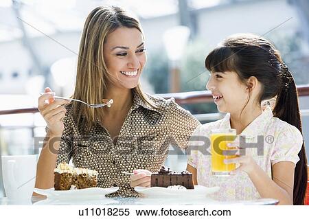 Stock Photography - Mother at restaurant with daughter eating dessert and smiling (selective focus). Fotosearch
