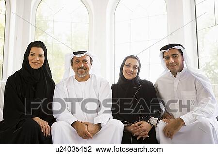 Stock Image - Two couples sitting in living room smiling (high key/selective focus). Fotosearch