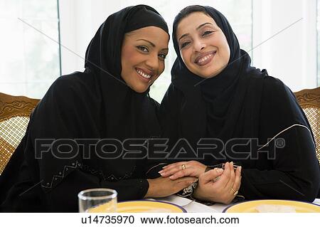 Stock Image - Two women sitting at dinner table smiling (high key). Fotosearch