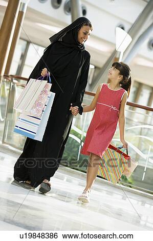 Stock Photograph - Woman and young girl walking in mall smiling (selective focus). Fotosearch