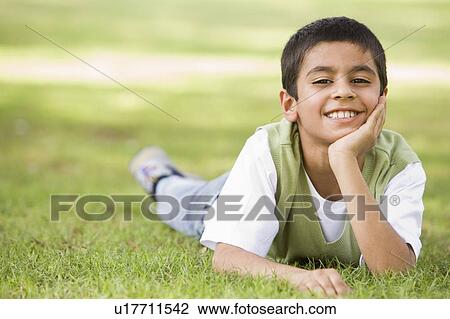 Stock Image - Young boy outdoors lying in grass and smiling (selective focus). Fotosearch