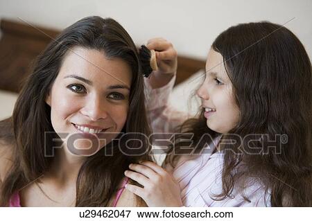 Stock Photo - Young girl brushing woman's hair on bed in bedroom smiling (selective focus). Fotosearch