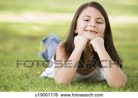 Young girl outdoors lying in grass and smiling (selective focus) View Large Photo Image Stock Photograph - Young girl outdoors lying in grass and smiling (selective focus). Fotosearch