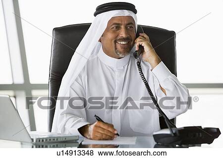 Stock Photo - Businessman in office on telephone by laptop smiling (high key/selective focus). Fotosearch