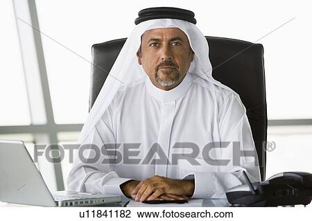Stock Image - Businessman in office with laptop (high key/selective focus). Fotosearch