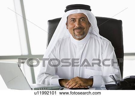 Stock Image - Businessman in office with laptop smiling (high key/selective focus). Fotosearch