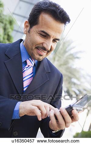 Stock Photo - Businessman outdoors using personal digital assistant and smiling (high key/selective focus). Fotosearch