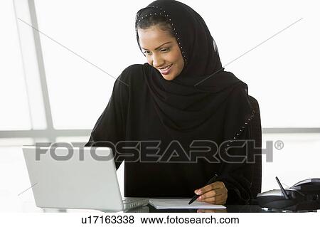 Businesswoman in office with laptop writing and smiling (high key/selective focus) View Large Photo Image Stock Photo - Businesswoman in office with laptop writing and smiling (high key/selective focus). Fotosearch