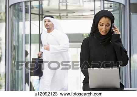 Businesswoman sitting outdoors by building with laptop using cellular phone with businessman running in background (selective focus) View Large Photo Image Stock Image - Businesswoman sitting outdoors by building with laptop using cellular phone with businessman running in background (selective focus). Fotosearch