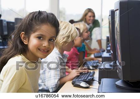 Picture - Children at computer terminals with teacher in background (depth of field/high key). Fotosearch