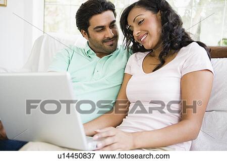 Stock Photo - Couple in living room with laptop smiling (high key/selective focus). Fotosearch