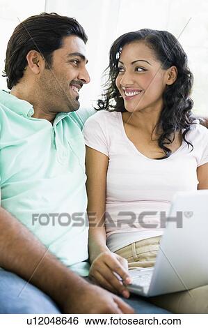 Couple in living room with laptop smiling (high key/selective focus) View Large Photo Image Stock Photograph - Couple in living room with laptop smiling (high key/selective focus). Fotosearch