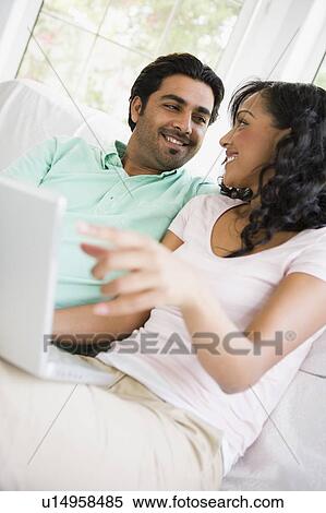 Couple in living room with laptop smiling (high key/selective focus) View Large Photo Image Stock Photography - Couple in living room with laptop smiling (high key/selective focus). Fotosearch