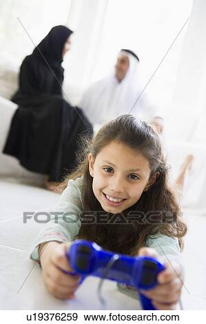 Daughter in living room playing video games smiling with parents in background (high key/selective focus) View Large Photo Image Stock Photo - Daughter in living room playing video games smiling with parents in background (high key/selective focus). Fotosearch