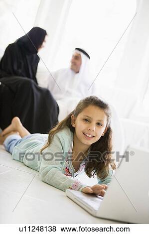 Daughter in living room using laptop and smiling with parents in background (high key/selective focus) View Large Photo Image Stock Photo - Daughter in living room using laptop and smiling with parents in background (high key/selective focus). Fotosearch