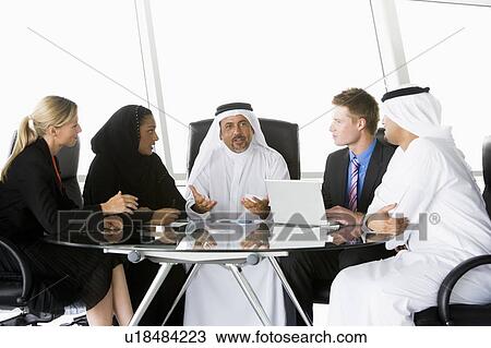 Stock Image - Five businesspeople in office with laptop talking and smiling (high key/selective focus). Fotosearch
