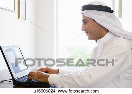 Picture - Man in office with laptop smiling (high key/selective focus). Fotosearch