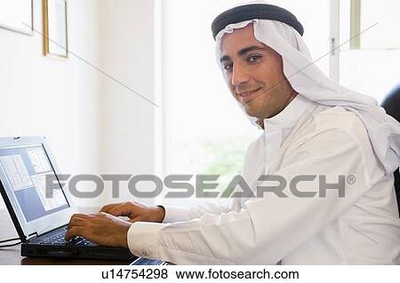 Stock Photo - Man in office with laptop smiling (high key/selective focus). Fotosearch
