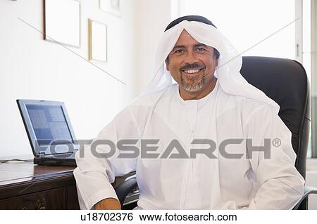 Stock Photograph - Man in office with laptop smiling (high key/selective focus). Fotosearch