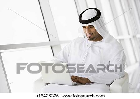 Stock Photograph - Man indoors with laptop smiling (high key/selective focus). Fotosearch