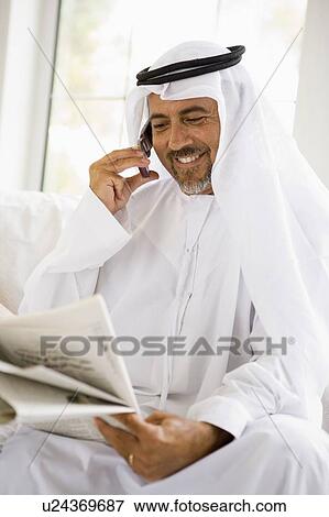Stock Photo - Man sitting indoors with newspaper and cellular phone smiling (high key/selective focus). Fotosearch