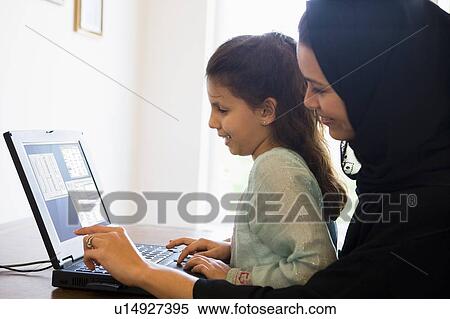 Stock Photography - Mother and daughter in office with laptop smiling (high key/selective focus). Fotosearch