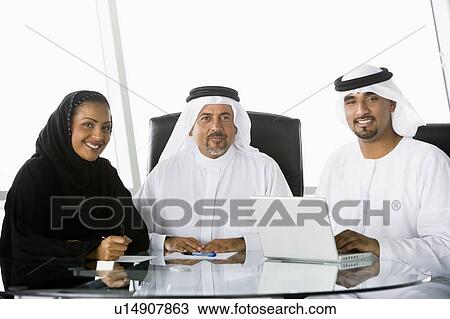 Stock Image - Three businesspeople in office with laptop smiling (high key/selective focus). Fotosearch