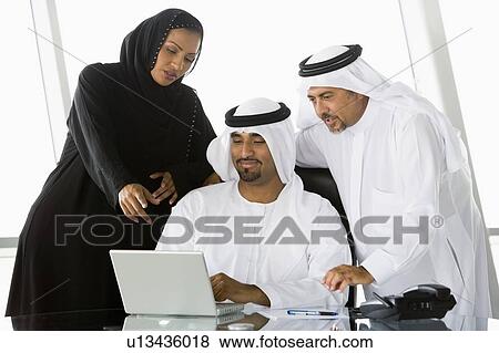 Stock Photo - Three businesspeople in office with laptop pointing and smiling (high key/selective focus). Fotosearch