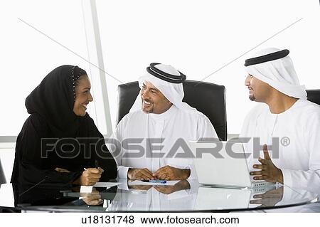 Three businesspeople in office with laptop talking and smiling (high key/selective focus) View Large Photo Image Stock Photo - Three businesspeople in office with laptop talking and smiling (high key/selective focus). Fotosearch