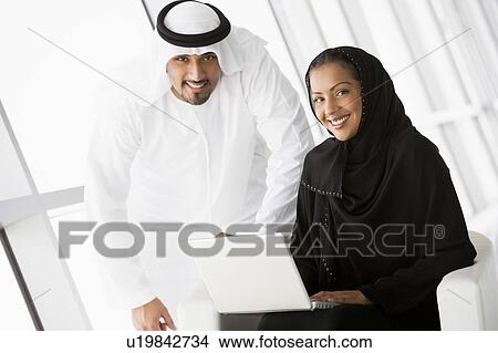 Picture - Two people indoors with laptop smiling (high key/selective focus). Fotosearch