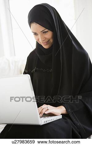 Stock Photo - Woman in living room on laptop smiling (high key/selective focus). Fotosearch