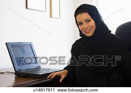 Stock Image - Woman in office with laptop smiling (high key/selective focus). Fotosearch