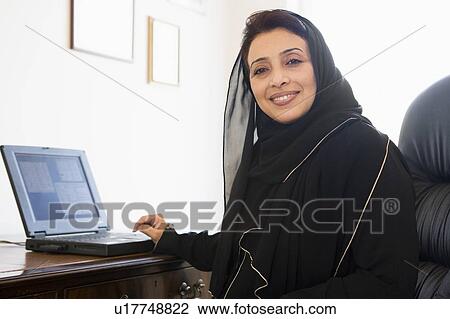 Stock Image - Woman in office with laptop smiling (high key/selective focus). Fotosearch