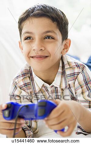 Stock Image - Young boy in living room playing video games and smiling (high key/selective focus). Fotosearch
