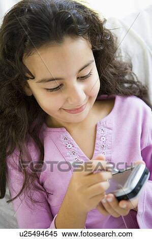 Stock Photography - Young girl in living room with personal digital assistant smiling (high key/selective focus). Fotosearch