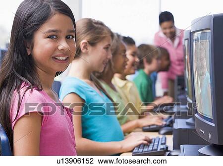Stock Image - Six children at computer terminals with teacher in background (depth of field/high key). Fotosearch