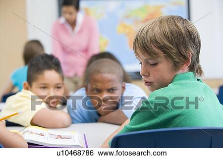 Stock Photograph - Student in class being bullied by students in background (selective focus). Fotosearch
