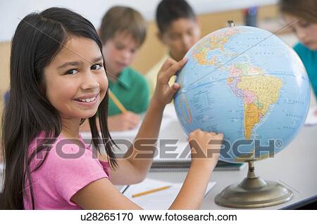 Stock Image - Student in class pointing at a globe (selective focus). Fotosearch