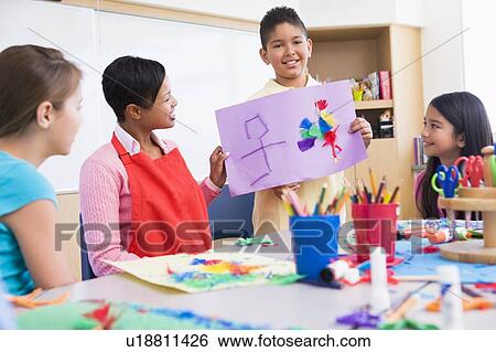 Stock Photograph - Student showing teacher and classmates his artwork (selective focus). Fotosearch
