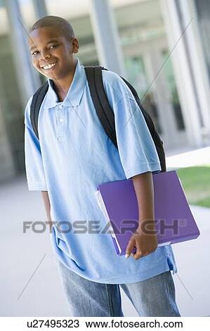 Stock Image - Student standing outside school holding binder and smiling (selective focus). Fotosearch