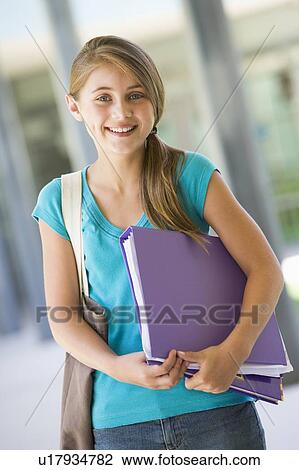 Stock Image - Student standing outside school with binder smiling (selective focus). Fotosearch