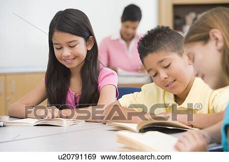 Stock Photo - Students in class reading with teacher in background (selective focus). Fotosearch